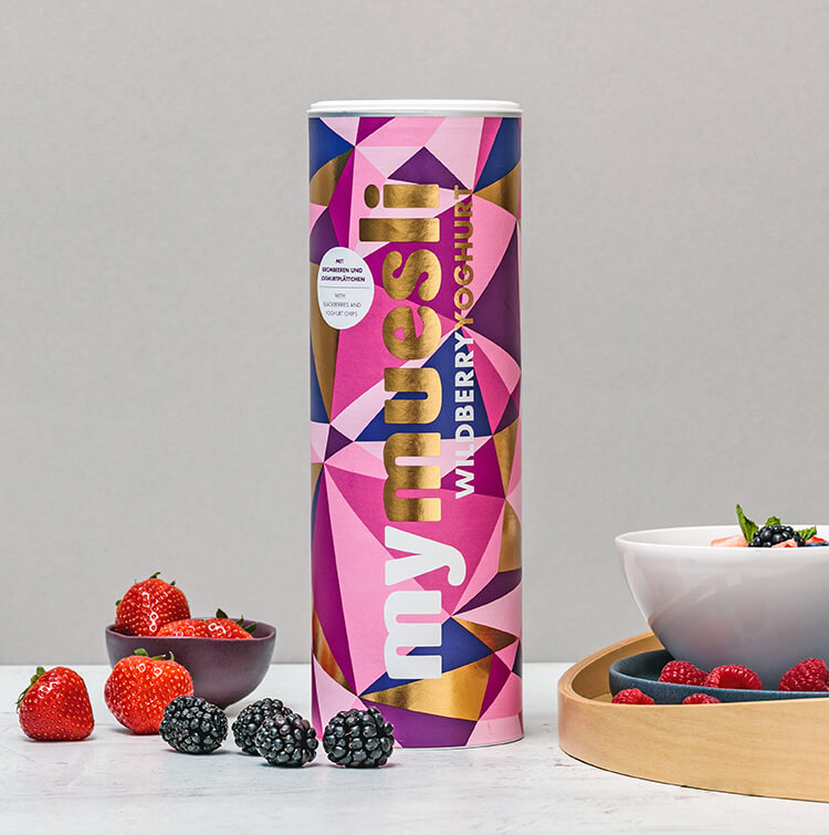 mymuesli Wildberry Yoghurt Muesli Dose mit Goldelementen und Rosatoenen neben frischen Erdbeeren und Brombeeren 